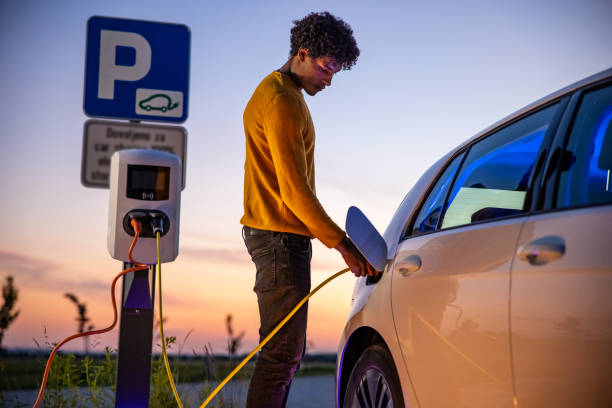 African American man plugging a charger into his EV with a sunset background